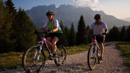 EGGENER TOUR © Exploring GmbH Two people mountain biking on a gravel path with mountains and trees in background