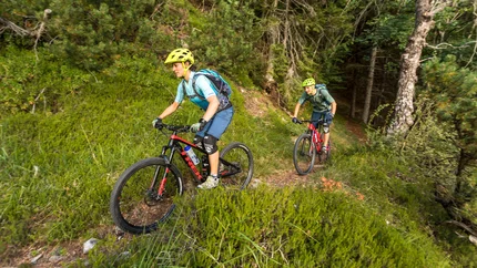 VAL DI SELLA © WOM Medien - Andreas Meyer Two mountain bikers cycling on a forest trail through green vegetation