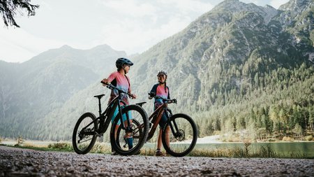 Quality Promise © Desire Lines - Tobias Dörr Two cyclists in colorful gear with helmets by a mountain lake