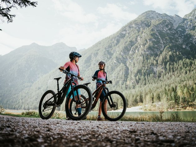 Quality Promise © Desire Lines - Tobias Dörr Two cyclists in colorful gear with helmets by a mountain lake