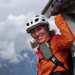 Mountain Bike Holidays © Hotel Innerhofer Frau mit Helm und orange Jacke beim Klettern an Holzstruktur in den Bergen