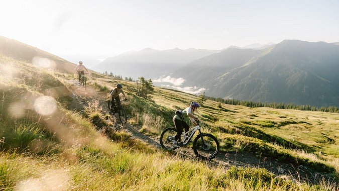Mountain Bike Holidays © saalbach.com, Moritz Ablinger Drei Mountainbiker fahren auf einem Bergpfad im Sonnenlicht