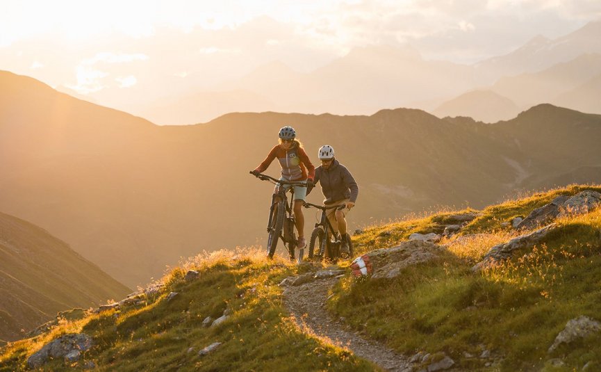 Mountain bike holidays in the 3 Zinnen Dolomites region © Elias Ochner - Stefan Schwabl Two mountain bikers riding on a trail in the mountains at sunset