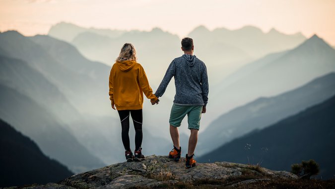 Mountain Bike Holidays © TVB Paznaun Ischgl Paar hält Händchen auf Berggipfel mit Nebel und Bergpanorama im Hintergrund