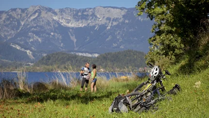 De Salzkammergut Tour © Landhotel Agathawirt Schenner Gesbr. Fietsen en rugzak op gras met twee wandelaars en bergen op de achtergrond