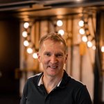 Mountain Bike Holidays © Hotel Traminerhof Mann lehnt sich an einen Tisch in einem warm beleuchteten Raum