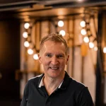 Mountain Bike Holidays © Hotel Traminerhof Mann lehnt sich an einen Tisch in einem warm beleuchteten Raum