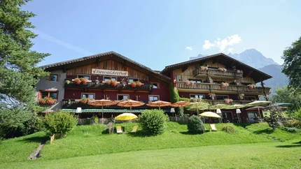 Hotel Ehrwalderhof © Hotel Ehrwalderhof Bauernhof mit Blumen, Sonnenschirmen und Bergen unter klarem Himmel