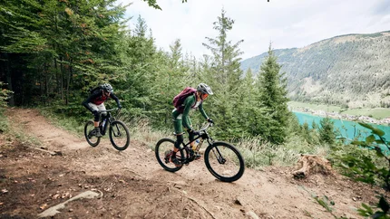 Tocht naar het sterrenbalkon © Tobias Köhler Twee mountainbikers op een bospaadje met uitzicht op bergen en een meer