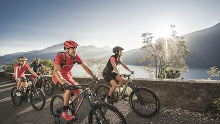 Lake Ledro © APT Garda Dolomiti Group of cyclists riding mountain bikes on road with lake view at sunset