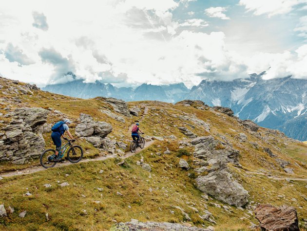 Quality Promise © David Karg Two mountain bikers riding on a rocky mountain trail under cloudy sky