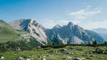 Dolomites UNESCO Nature Park Tour © Moritz Hübner Green meadow with rocks in front of steep mountains under blue sky