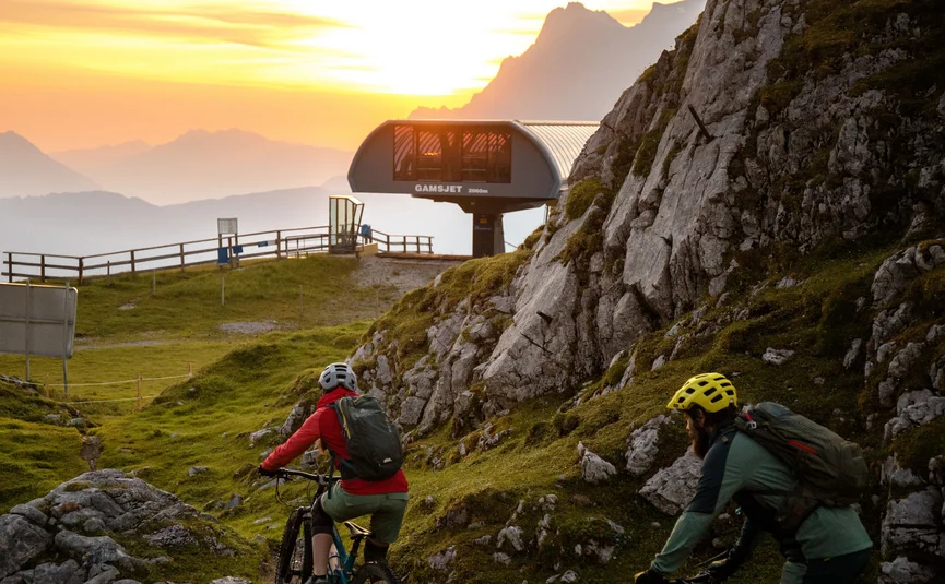 Mountain bike holidays in the Tiroler Zugspitz Arena © David Karg Two mountain bikers riding past a mountain cable car station at sunset
