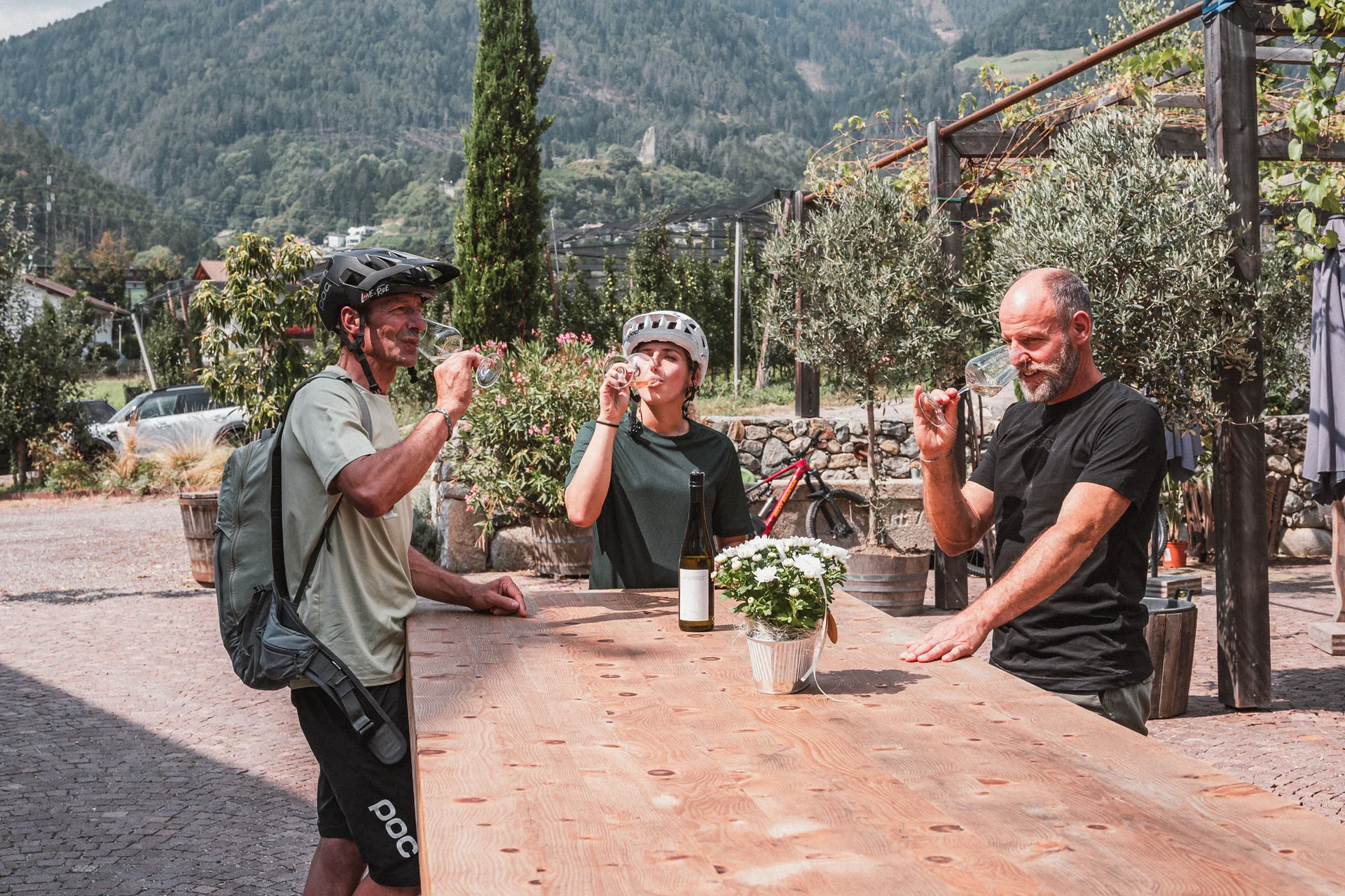 Mountain Bike Holidays © Brixen Tourismus - Hannes Engl Drei Radfahrer trinken Wein im Freien vor Berglandschaft