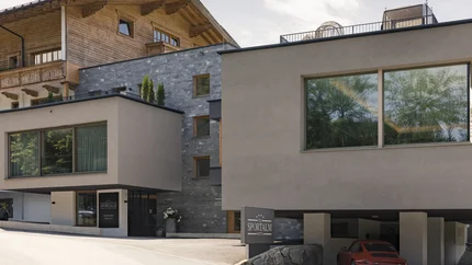 Geniesserhotel Minglers Sportalm © Jenny Haimerl Modernes Hotel mit Kombination aus Holz- und Stein Fassade und rotem Auto vor der Garage