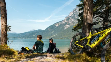 SEEBENSEE TOUR © David Karg Two cyclists sitting by a lake with mountains in the background