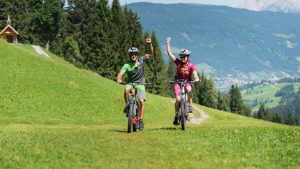 Sattelbauer MTB Tour © Salzburger Sportwelt - Christian Scharttner Two cyclists riding on a grassy mountain trail with raised arms