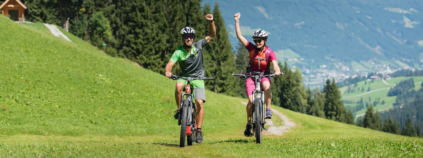 Sattelbauer MTB Tour © Salzburger Sportwelt - Christian Scharttner Two cyclists riding on a grassy mountain trail with raised arms