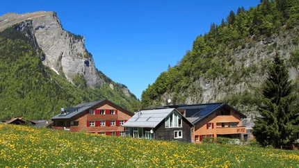 Alpen Hotel Post © Alpen Hotel Post Alpenhütte mit gelben Blumenfeld und steilen Felsen unter klarem blauem Himmel