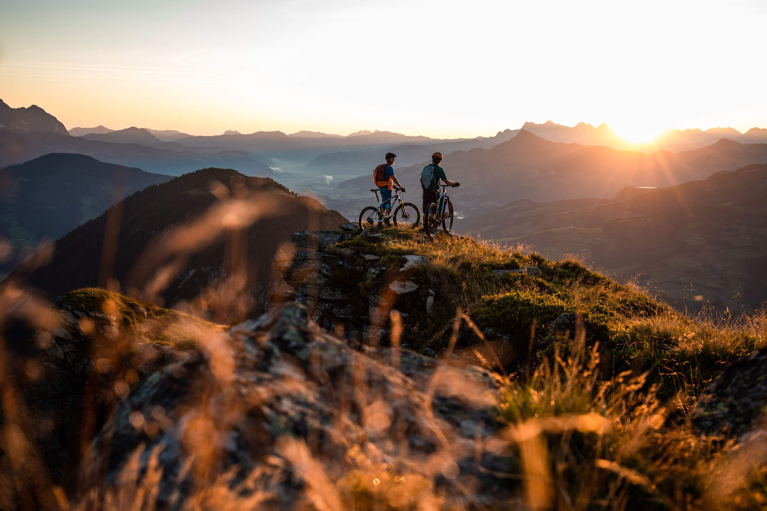 BRECHHORN © TVB Kitzbüheler Alpen Brixental - Mathäus Gartner Two mountain bikers on a summit watching the sunset