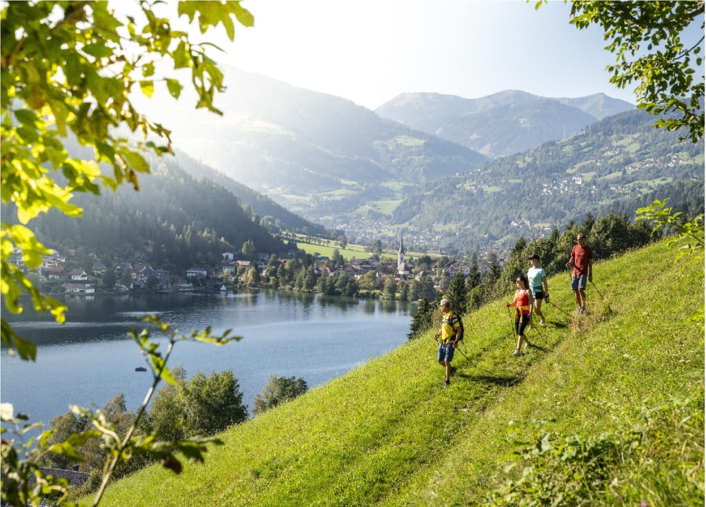 Springtime 4=3 Hikers walking on green hillside with mountain and lake view