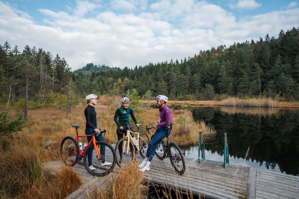 Gravel safari Three cyclists standing with bikes on a wooden pier by a lake in autumn forest